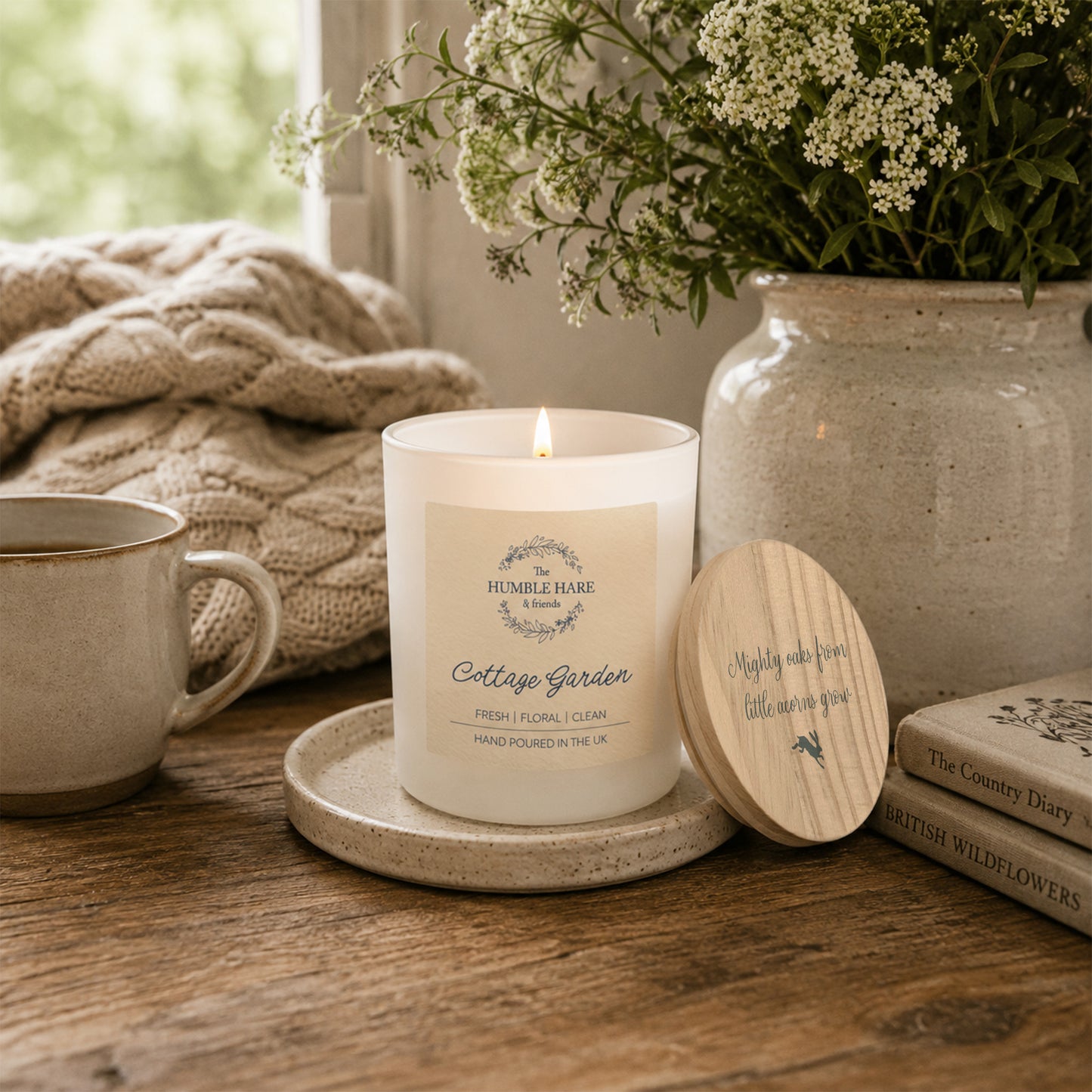 A white glass candle jar with a light wood lid with the quote 'Mighty oaks from little acorns grow' and a small leaping hare silhouette.