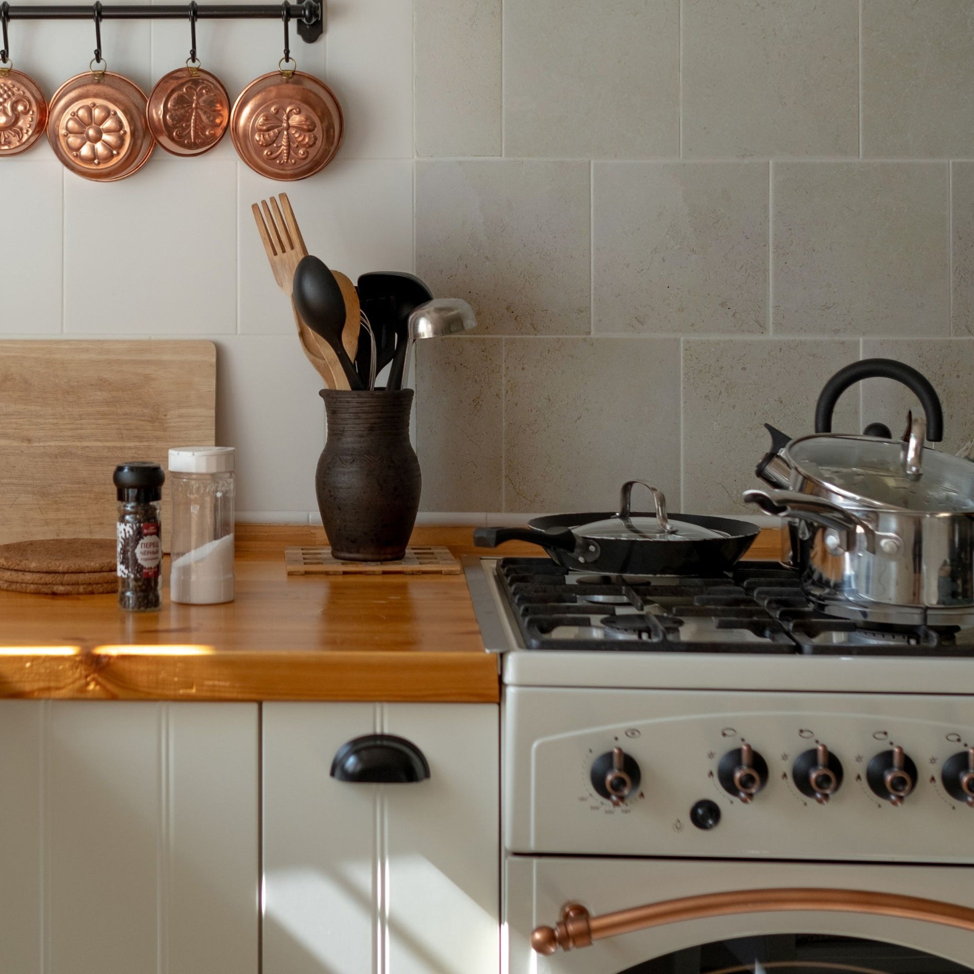 A tiled splashback behind an oven in a country kitchen. The splashback is made up of medium plain cream marble tiles.