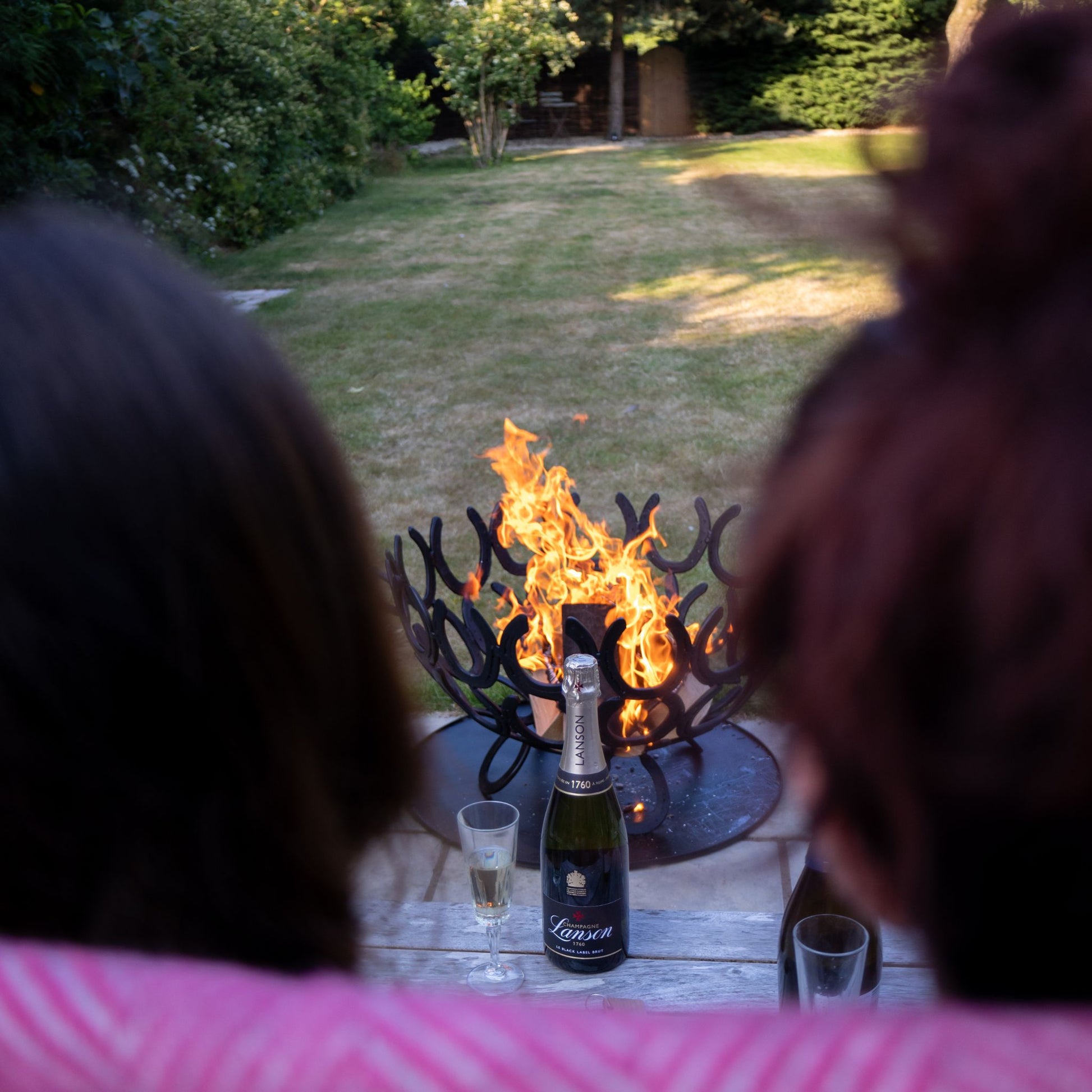 Two women sat in front of a fire in a handmade horseshoe fire pit on a patio in a country garden.