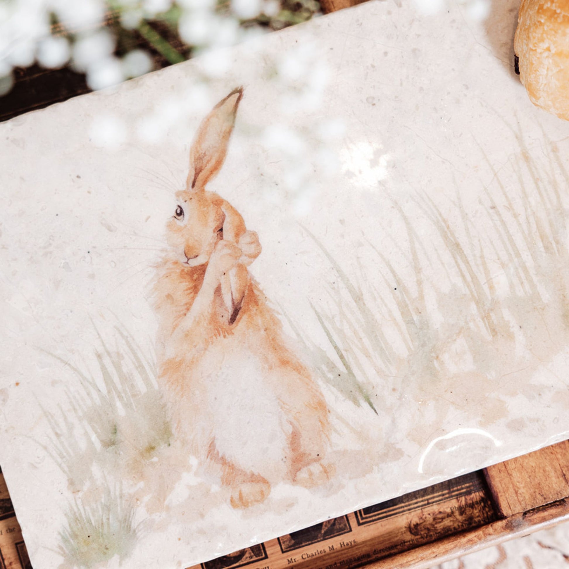 A closeup of a watercolour design on a marble sharing platter, showing a hare in long grass washing his ear.