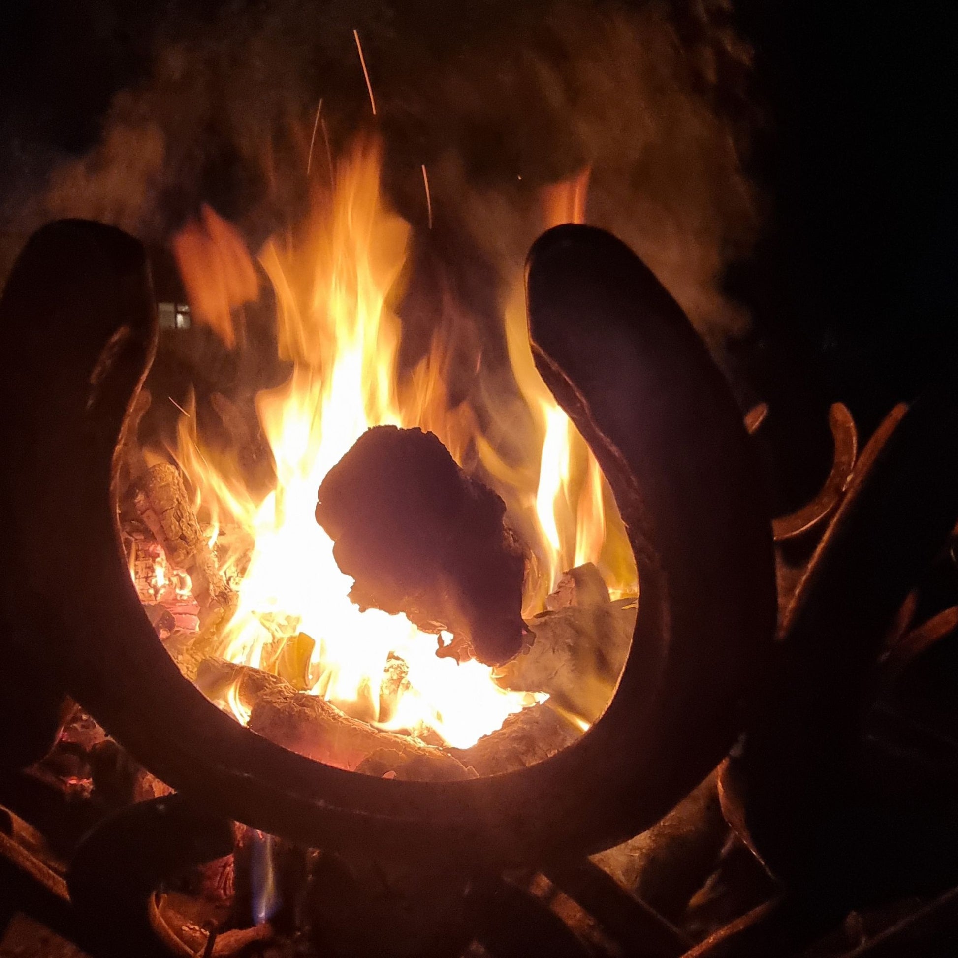 A closeup of wood on fire in a handmade horseshoe fire pit.