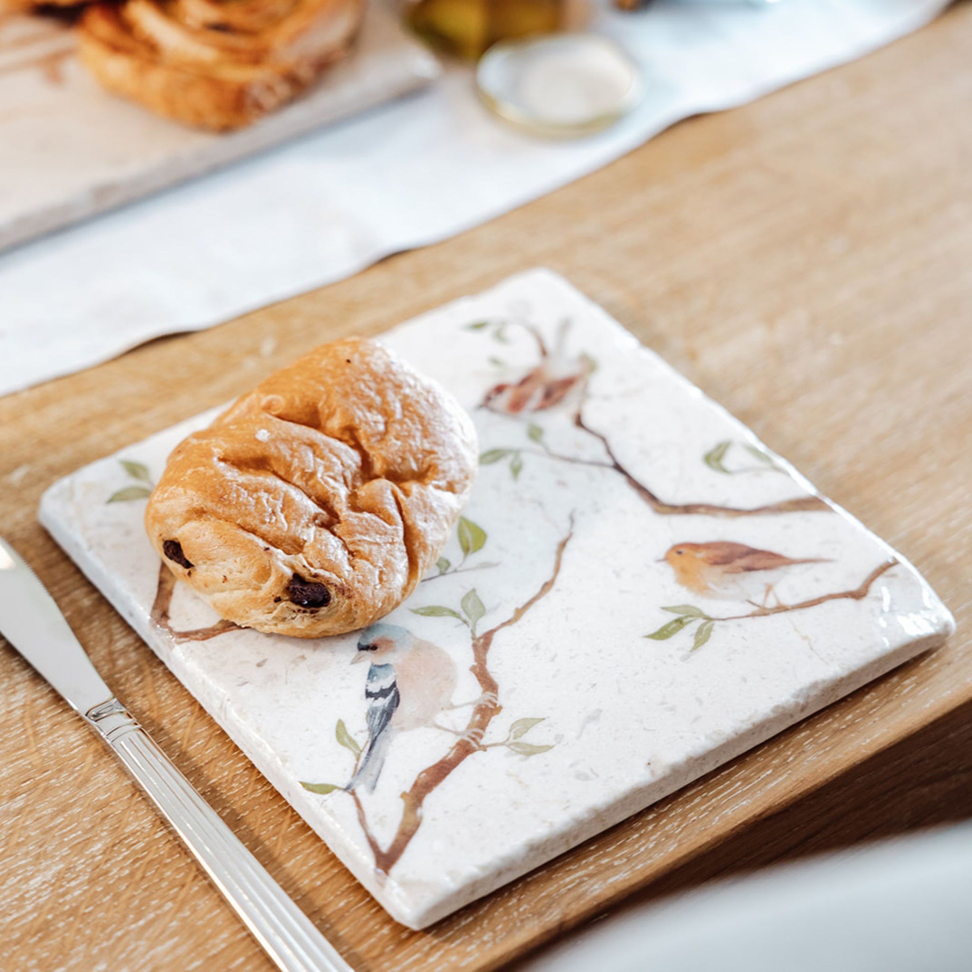 A medium multipurpose marble platter with a watercolour design featuring British garden birds on branches. The platter is being used as a plate for breakfast pastries.
