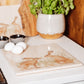 A large square marble platter on a country kitchen worksurface. The platter features a watercolour design of two hares facing each other about to touch noses.