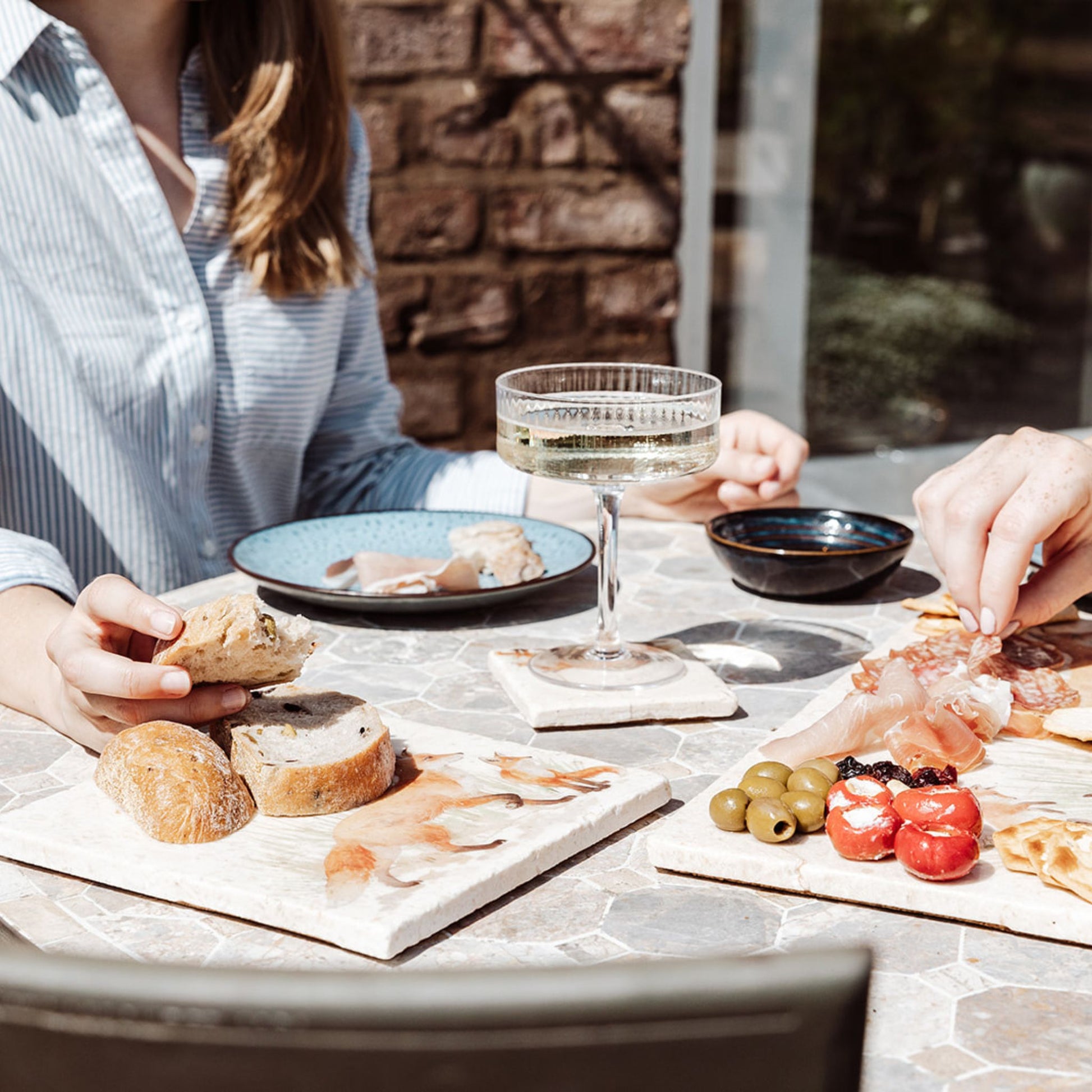 A sunny garden table set for outdoor dining with marble platters featuring a fox and fox cub design. The platters are being used as a breadboard and a charcuterie board. 