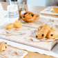 A breakfast table set with a marble sharing platter featuring British garden birds on branches in a watercolour style. The platter is being used to serve pastries and fruit.