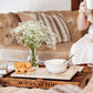 A cosy farmhouse interior, with the focus on a cream marble sharing platter with breakfast pastries and a cereal bowl resting on it. The platter has a watercolour design featuring a hare washing his ear.