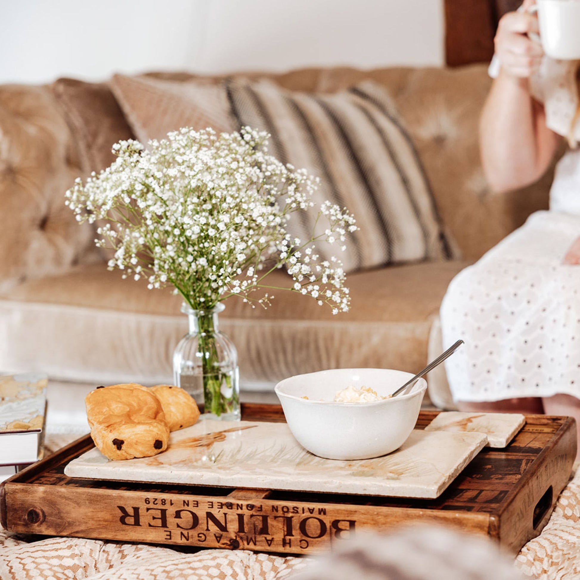 A cosy farmhouse interior, with the focus on a cream marble sharing platter with breakfast pastries and a cereal bowl resting on it. The platter has a watercolour design featuring a hare washing his ear.