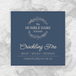 A square product label for 'The Humble Hare & friends' Crackling Fire' scented candle, featuring a dark blue background with elegant cream typography. The label is styled on a white textured background with a grey smoke effect behind it.