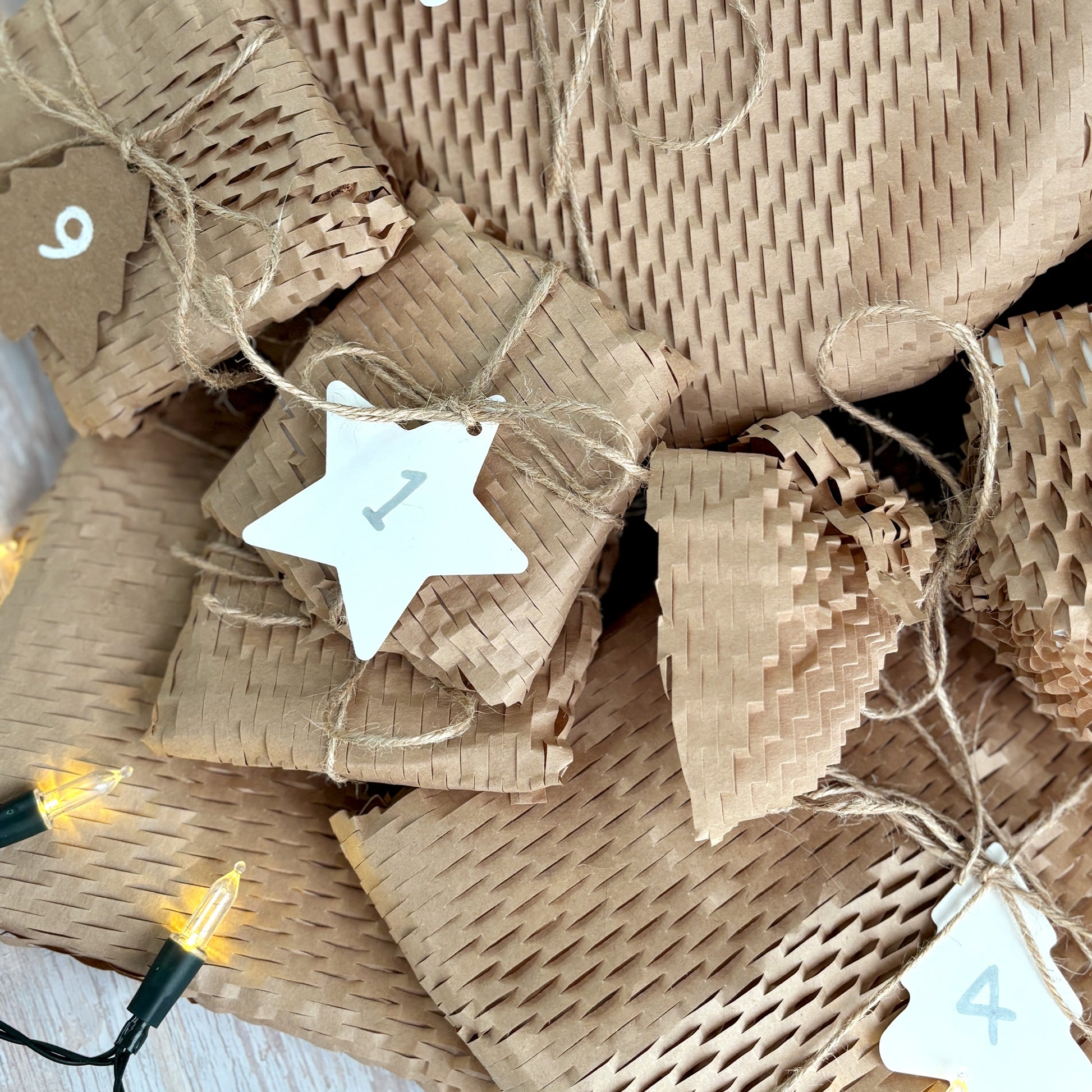 A 12 Days of Christmas homeware Advent Calendar under the tree, with each gift wrapped in rustic brown paper and twine, with numbered labels.