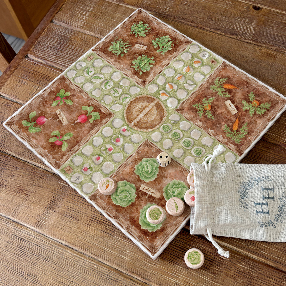 A marble Ludo board with an allotment theme, with vegetable wooden counters in a cotton drawstring bag. The game is set on a wooden farmhouse dining table.
