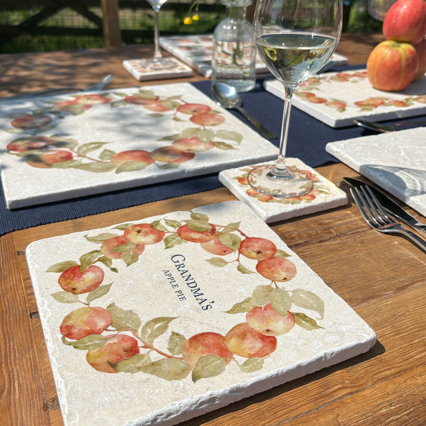 A personalised medium square marble platter featuring a watercolour apple wreath design. The platter is set on a dinner table next to a marble placemat and coaster.