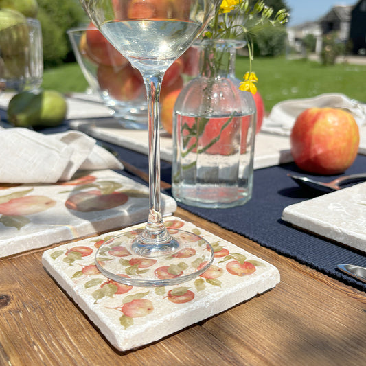 A handmade rustic marble coaster featuring a pattern of red apples, set on a garden dining table.