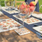 A table in a sunny garden set with marble placemats and coasters featuring a beautiful maximalist apple pattern.