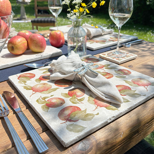 An al fresco dining table set with marble placemats and coasters featuring a maximalist apple pattern.