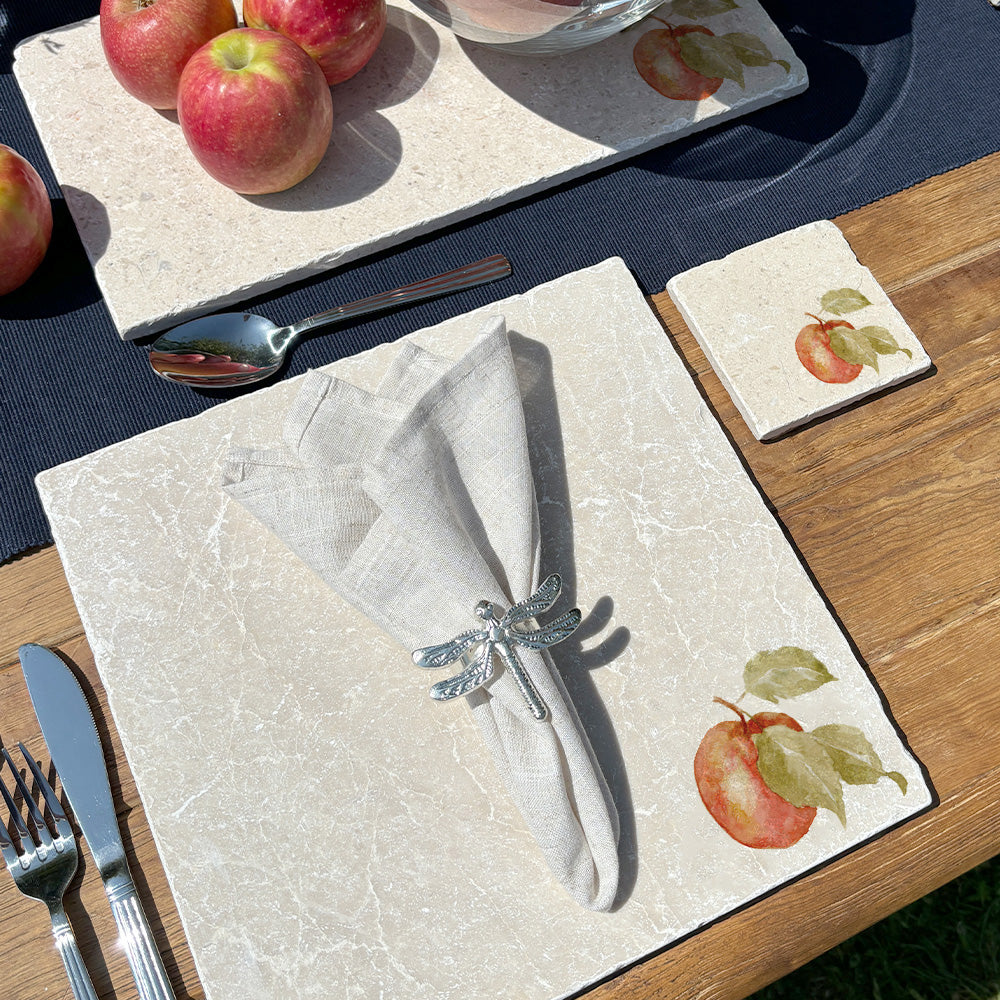 An al fresco dining table set with marble placemats and coasters featuring a minimalistic watercolour apple design.