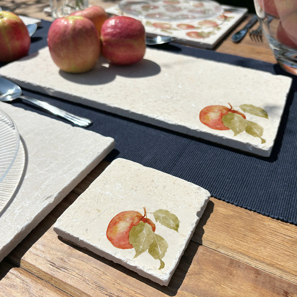 An al fresco dining table set with a square marble coaster featuring a minimalistic watercolour apple design.