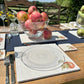 An al fresco dining table set with marble placemats and coasters featuring a minimalistic watercolour apple design.