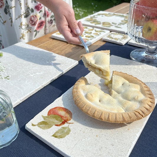 A marble sharing platter featuring a single apple watercolour design. The sharing board is being used to serve an apple pie to dinner guests.