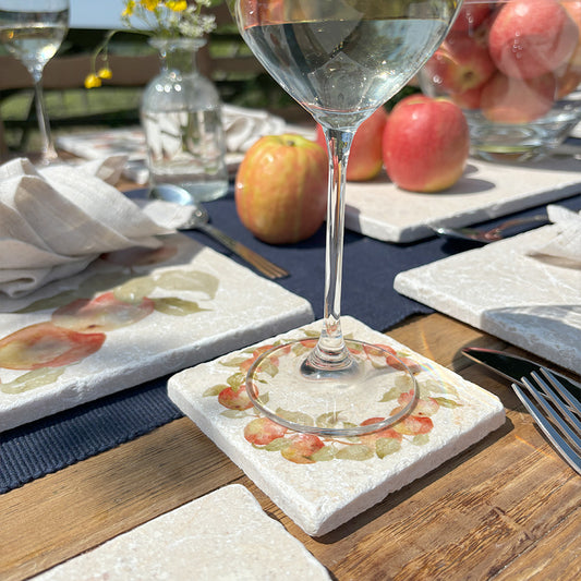 A handmade marble coaster featuring a wreath of apple branches. The coaster is set with an elegant wine glass on a dining table set for dinner guests.