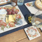 An al fresco dining table set with marble coasters and serving platters all featuring a watercolour apple wreath design.