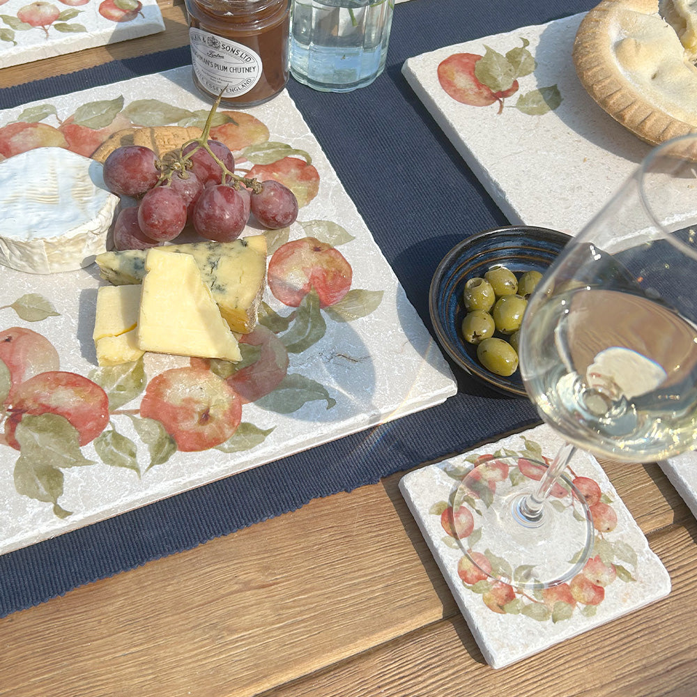 An al fresco dining table set with marble coasters and serving platters all featuring a watercolour apple wreath design.