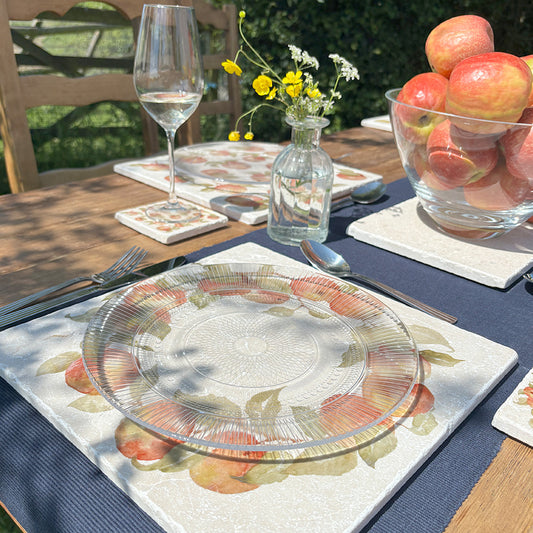 A garden table in the sunshine, the table is set with marble placemats and coasters featuring a rustic apple wreath design.