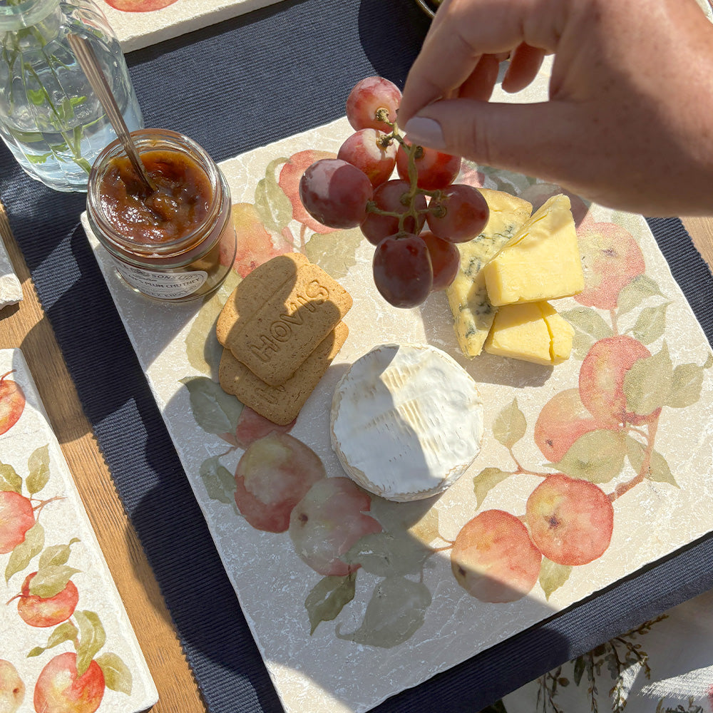 A large marble platter featuring a watercolour apple wreath design. The platter is being used as a serving board for cheese, crackers and chutney.