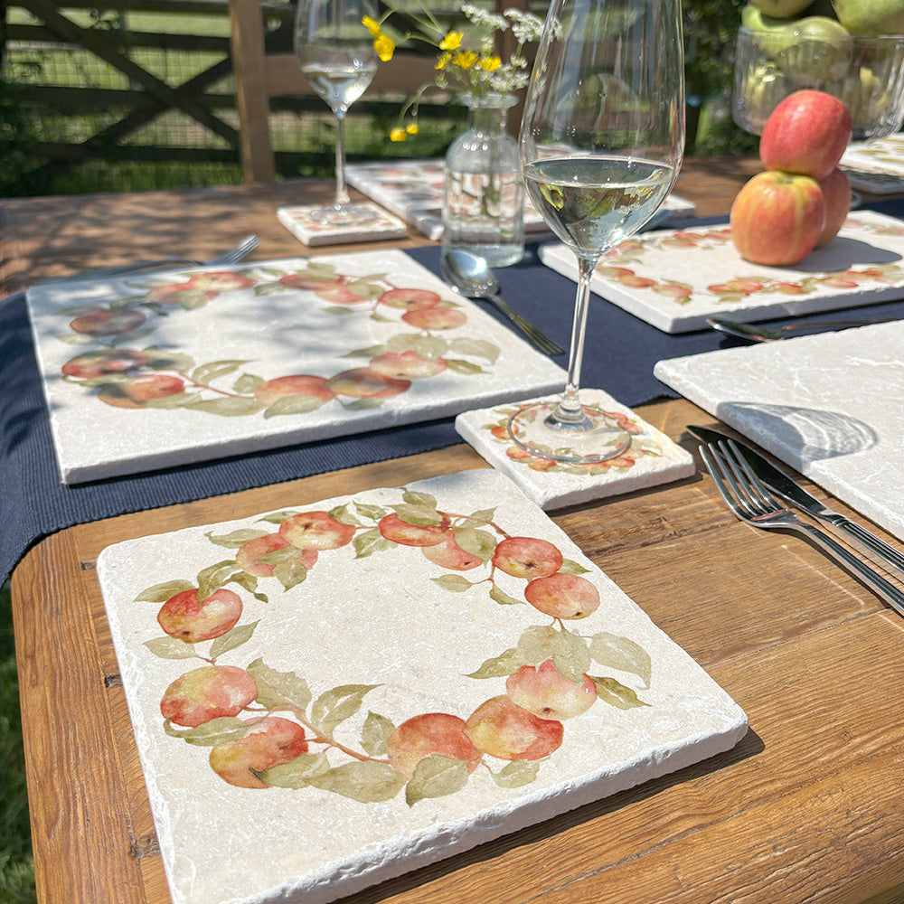 A medium square marble platter featuring a watercolour apple wreath design. The platter is set on a dinner table next to a marble placemat and coaster.