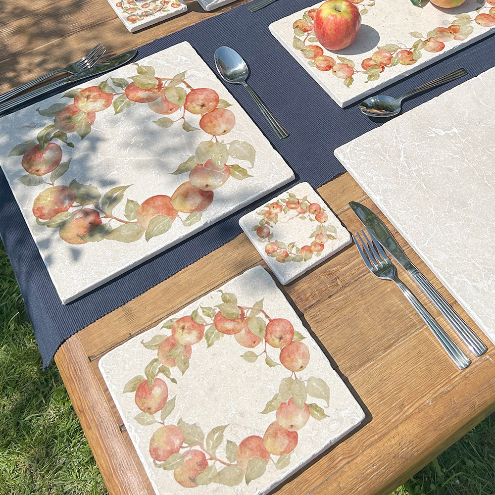 A medium square marble platter featuring a watercolour apple wreath design, the platter is on an al fresco dining table set for a summer soiree.