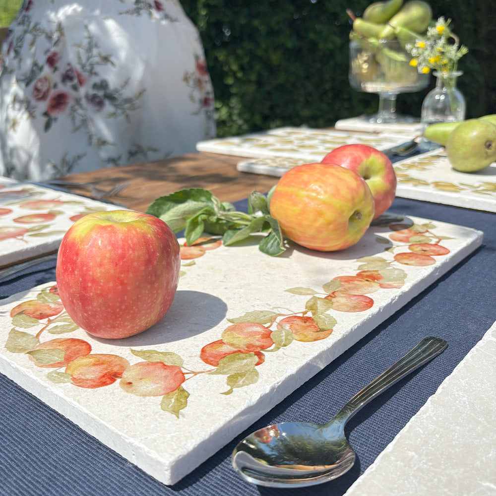 An al fresco dinner table in the garden, set with marble serving platters featuring a vintage apple wreath watercolour design.