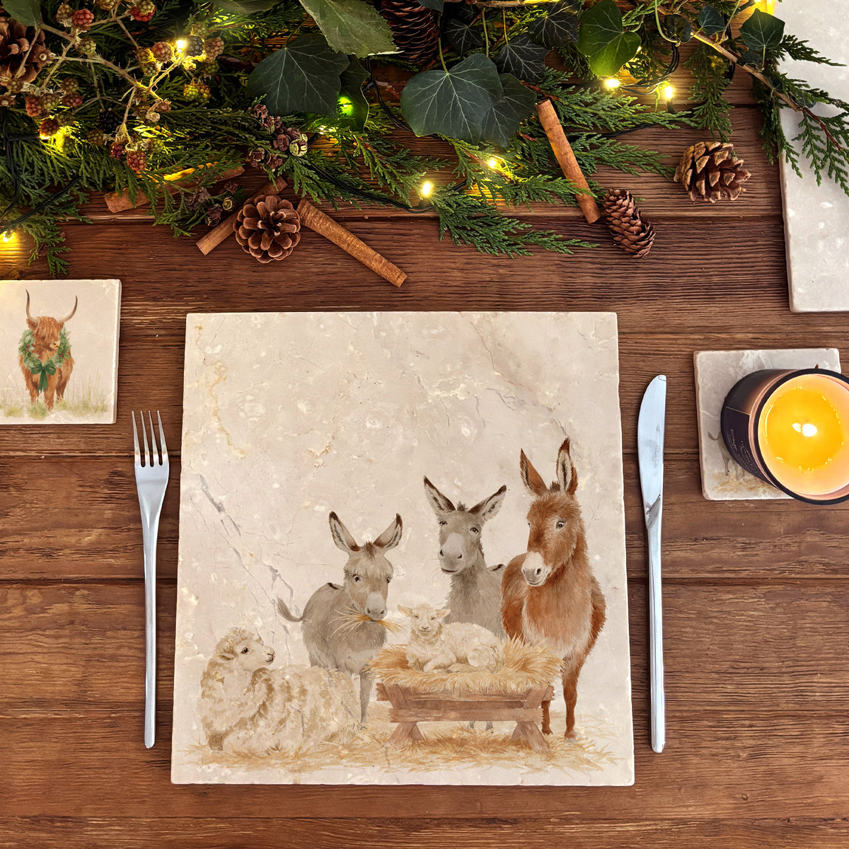 A large square marble platter featuring a rustic nativity scene illustration with three donkeys, a sheep, and a baby lamb in a wooden manger.
