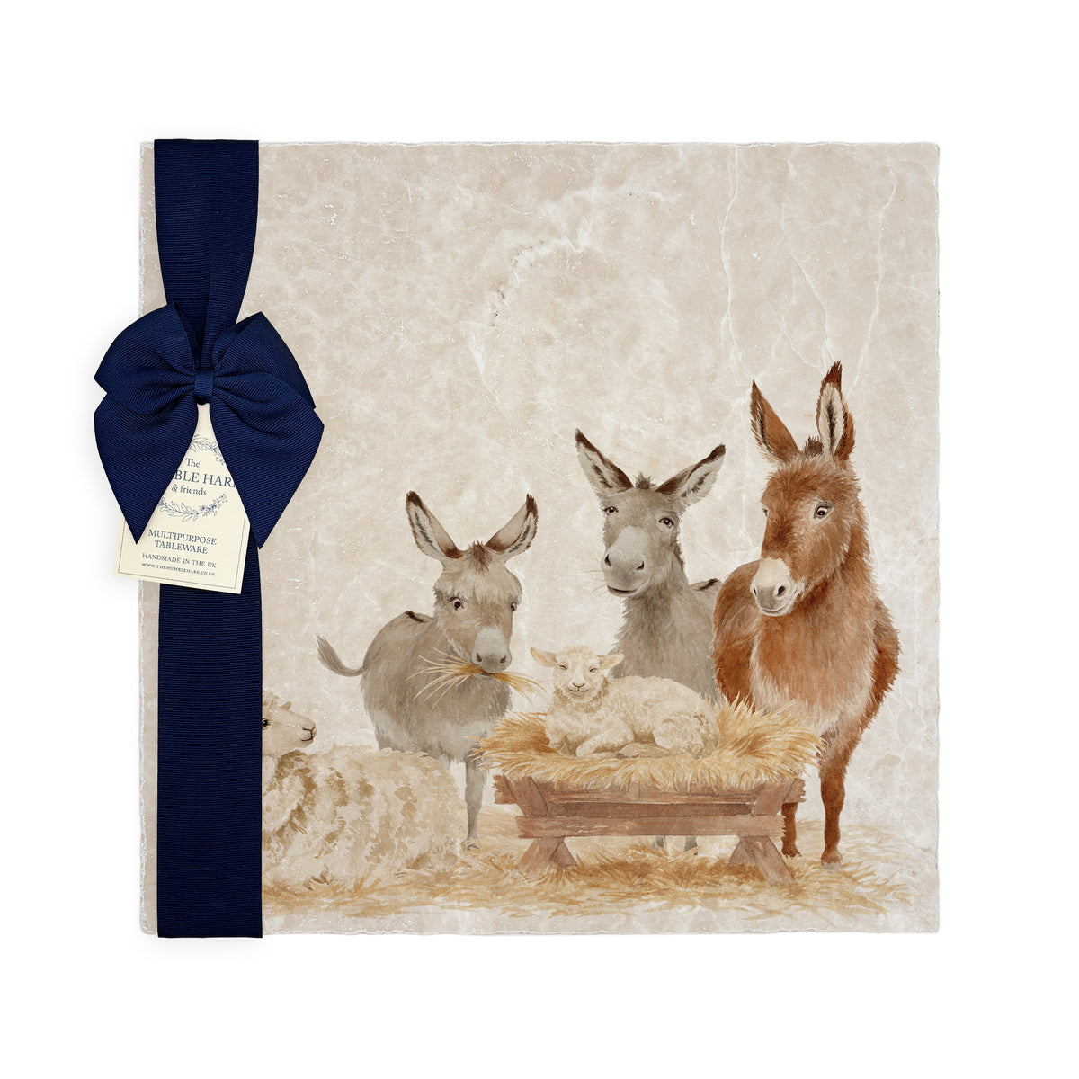A large square marble platter featuring a rustic nativity scene illustration with three donkeys, a sheep, and a baby lamb in a wooden manger, tied with a dark navy ribbon and small paper tag on a white background.