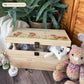 Large sized wooden pine personalised keepsake box. The design theme is perfect for New babies, Welcome to the world, baby showers and christenings. This design has baby highland cow calves in meadow style grass and a buzzy Bee flying around. The picture also shows an example in a nursey room filled with nappies, vests and teddys. 