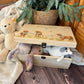 Large sized wooden pine personalised keepsake box. The design theme is perfect for New babies, Welcome to the world, baby showers and christenings. This design has baby highland cow calves in meadow style grass and a buzzy Bee flying around. The picture also shows an example in a nursey room filled with nappies, vests and teddys. 