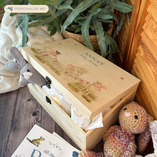 Large sized wooden pine personalised keepsake box. The design theme is perfect for New babies, Welcome to the world, baby showers and christenings. This design has baby lambs  in playing in grass with a little bee flying around.  The picture also shows an example in a nursey room filled with nappies, vests and teddys. 