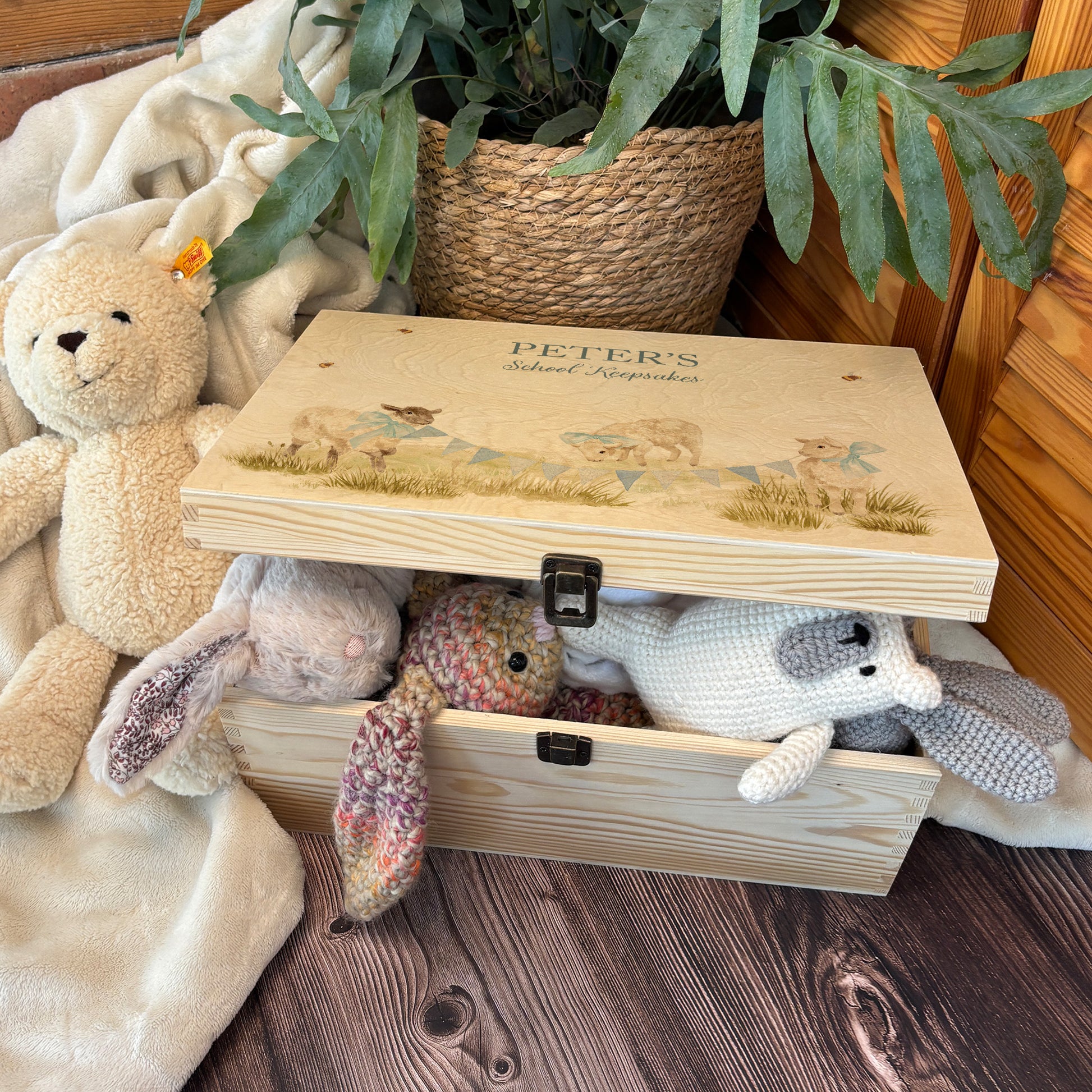 Large sized wooden pine personalised keepsake box. The design theme is perfect for New babies, Welcome to the world, baby showers and christenings. This design has baby lambs  in playing in grass with a little bee flying around.  The picture also shows an example in a nursey room filled with nappies, vests and teddys. 