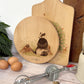 Round wooden chopping board on a kitchen worktop. The beech wood board features a badger and mole woodland animal design.