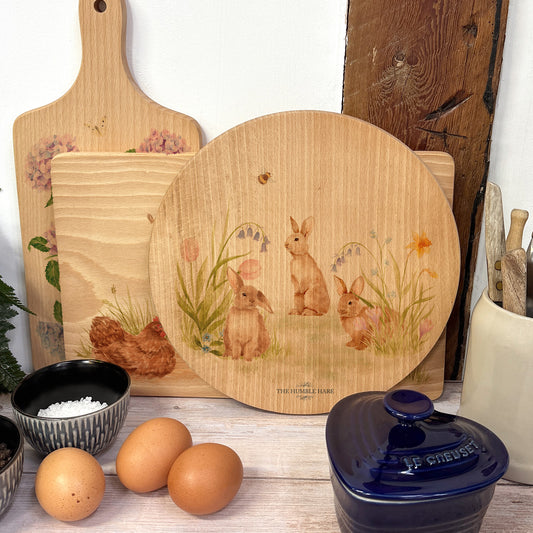 Round wooden chopping board on a kitchen worktop. The beech wood board features our blooming bunnies woodland animal design.
