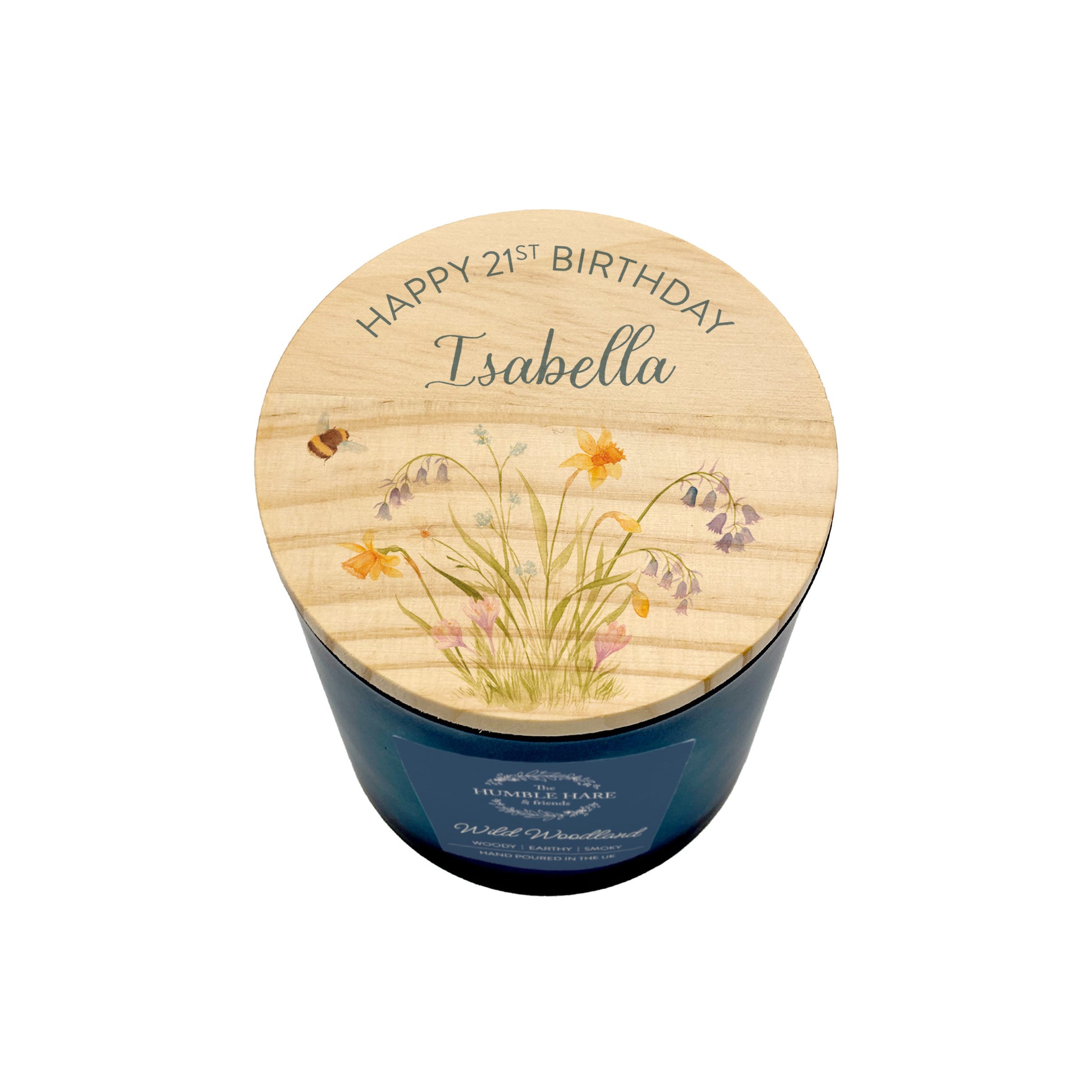 A personalised birthday candle in a dark blue glass jar with a light wood lid printed with 'HAPPY 21ST BIRTHDAY Isabella' and delicate wildflower illustrations, shown on a white background.