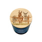 A blue glass jar candle with a round wooden lid featuring an illustration of three donkeys and a robin.