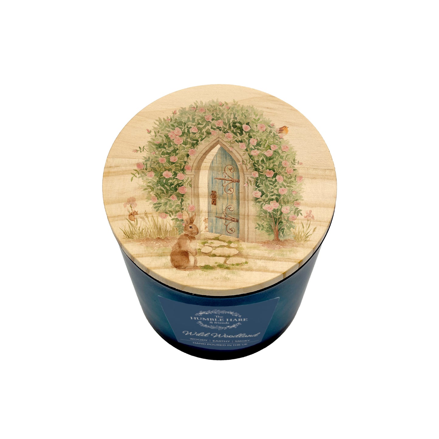 A blue cylindrical candle glass jar with a round wooden lid decorated with an illustration of a small rabbit sitting in front of a floral archway and arched door.