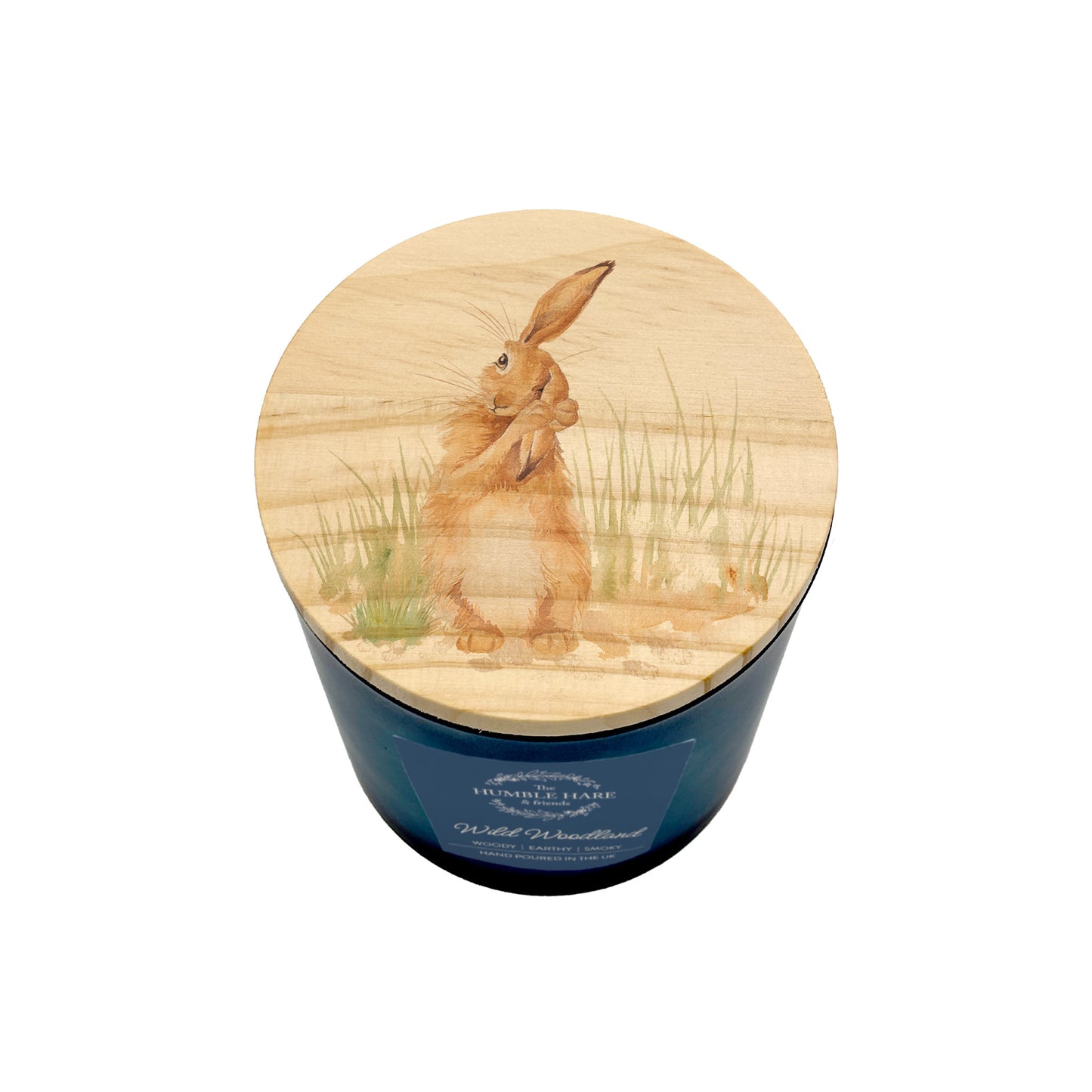 A blue glass jar candle with a round light wood lid featuring a painted brown hare washing his ear sitting in tall grass, shown on a white background.
