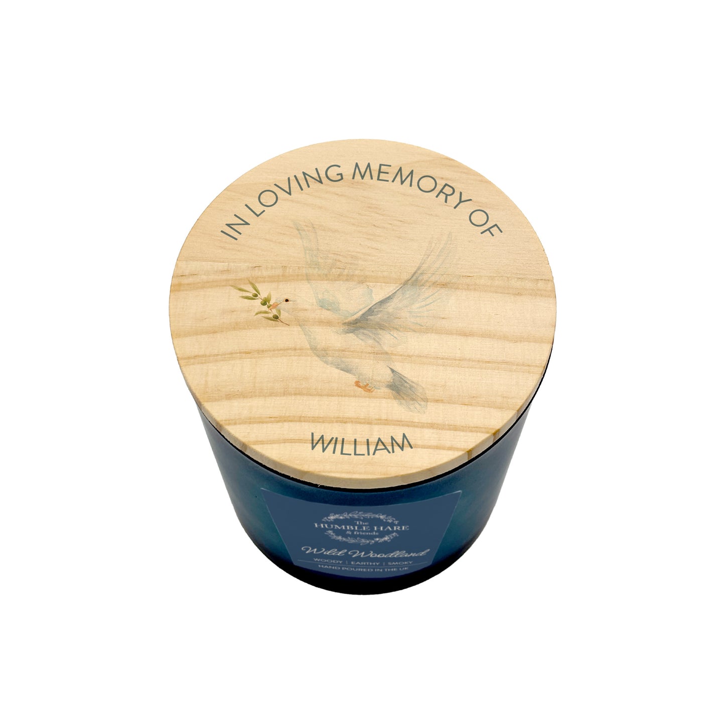 A memorial jar candle with a dark blue glass body and a light wood lid engraved with a dove, olive branch, and the text 'IN LOVING MEMORY OF WILLIAM'.