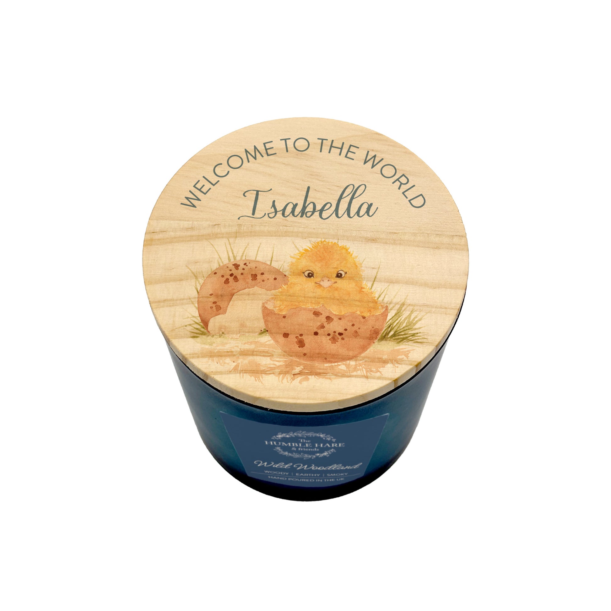 A personalized baby shower candle in a dark blue glass jar with a round wooden lid. The lid features an illustration of a yellow chick hatching from an egg and the text 'WELCOME TO THE WORLD Isabella'.