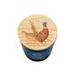 A blue glass jar candle with a round light wood lid featuring a detailed illustration of two pheasant birds in a grassy field, shown on a white background.