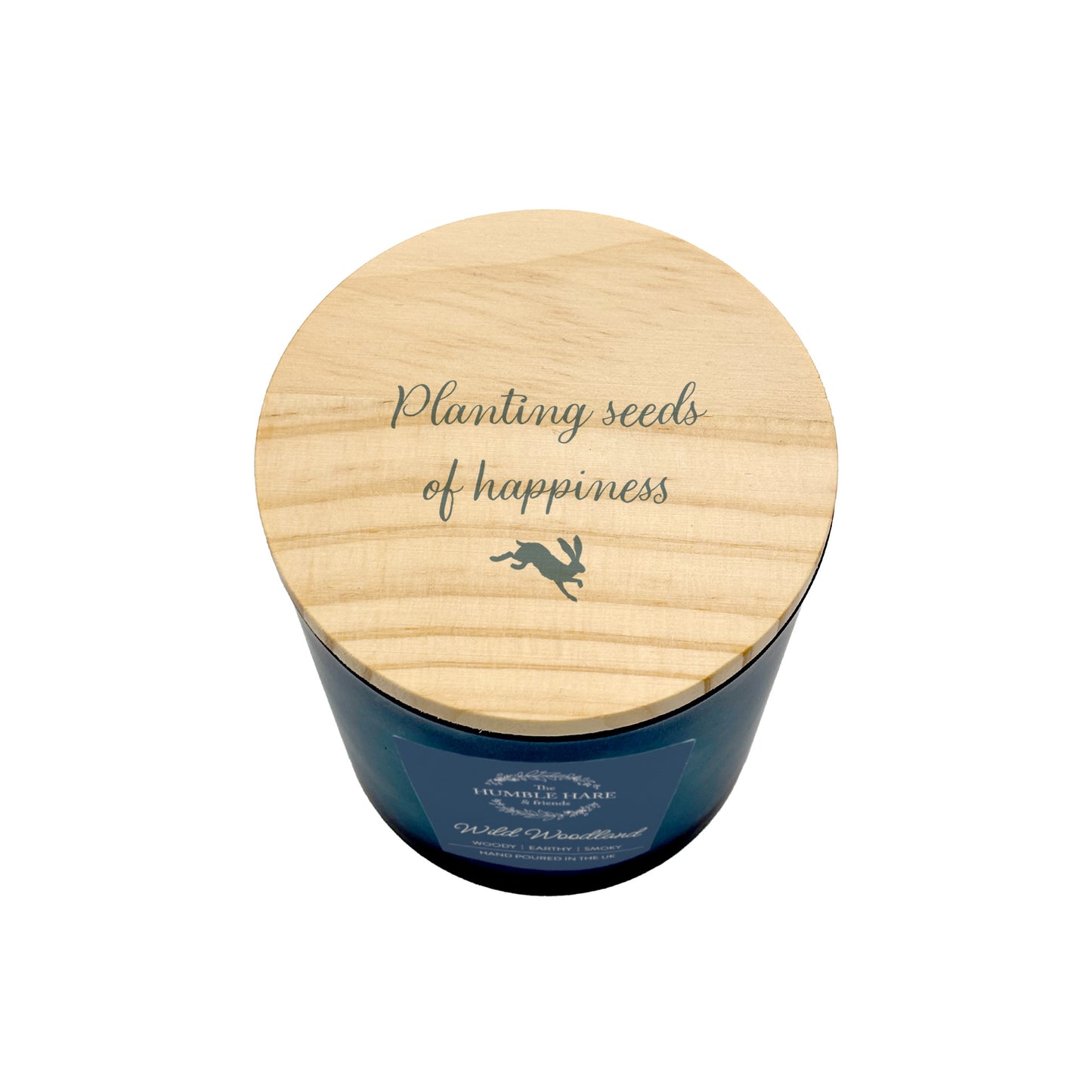 A dark blue glass jar candle with a light natural wood lid with the quote 'Planting seeds of happiness' and a small leaping hare silhouette.