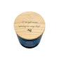 A dark blue glass jar candle with a round light wood lid with the phrase 'I've got some spring in my step!' and a small leaping hare silhouette, shown on a white background.