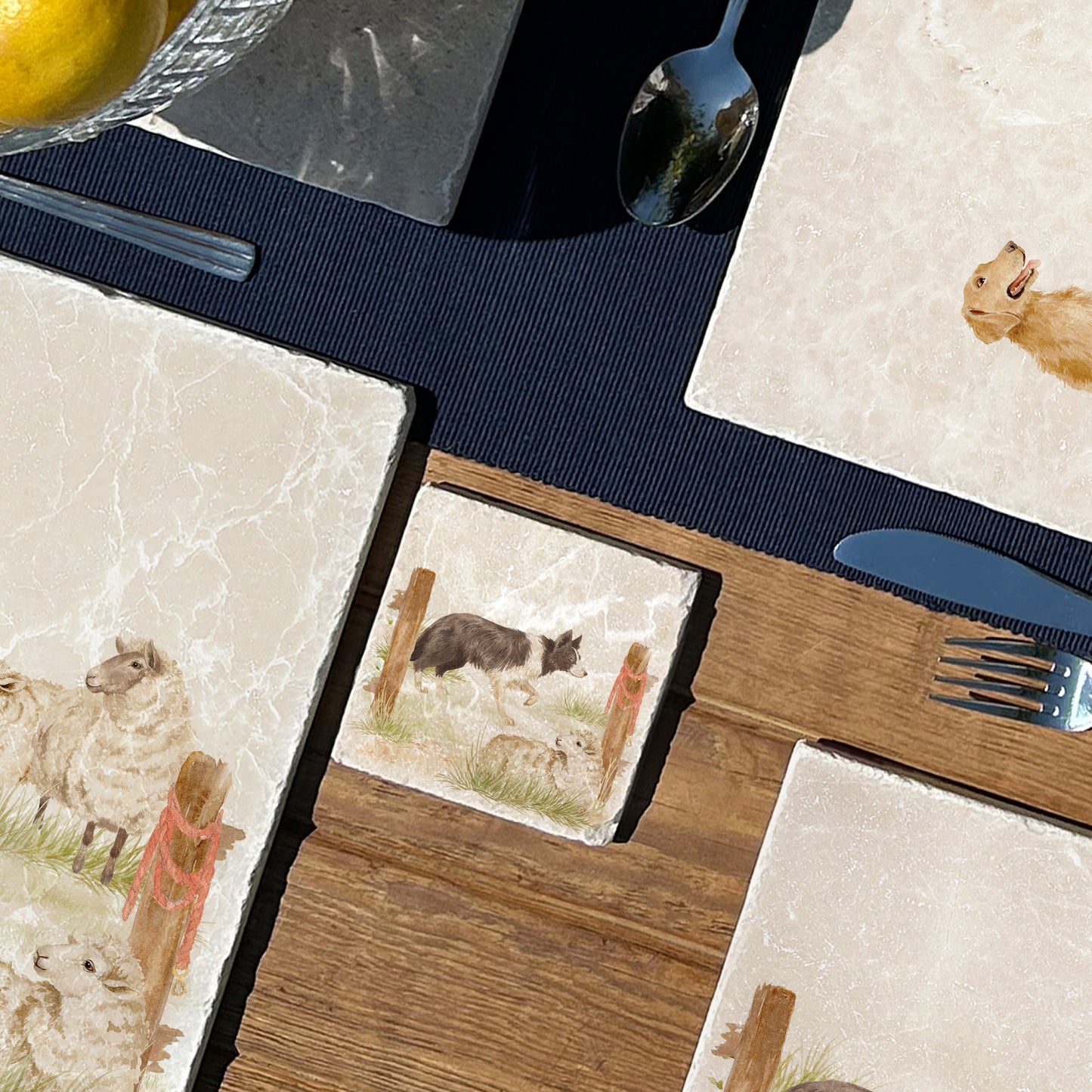 A square marble coaster with a design of a border collie working dog herding sheep through a gate on the farm. The coaster is set on a wooden country kitchen table.