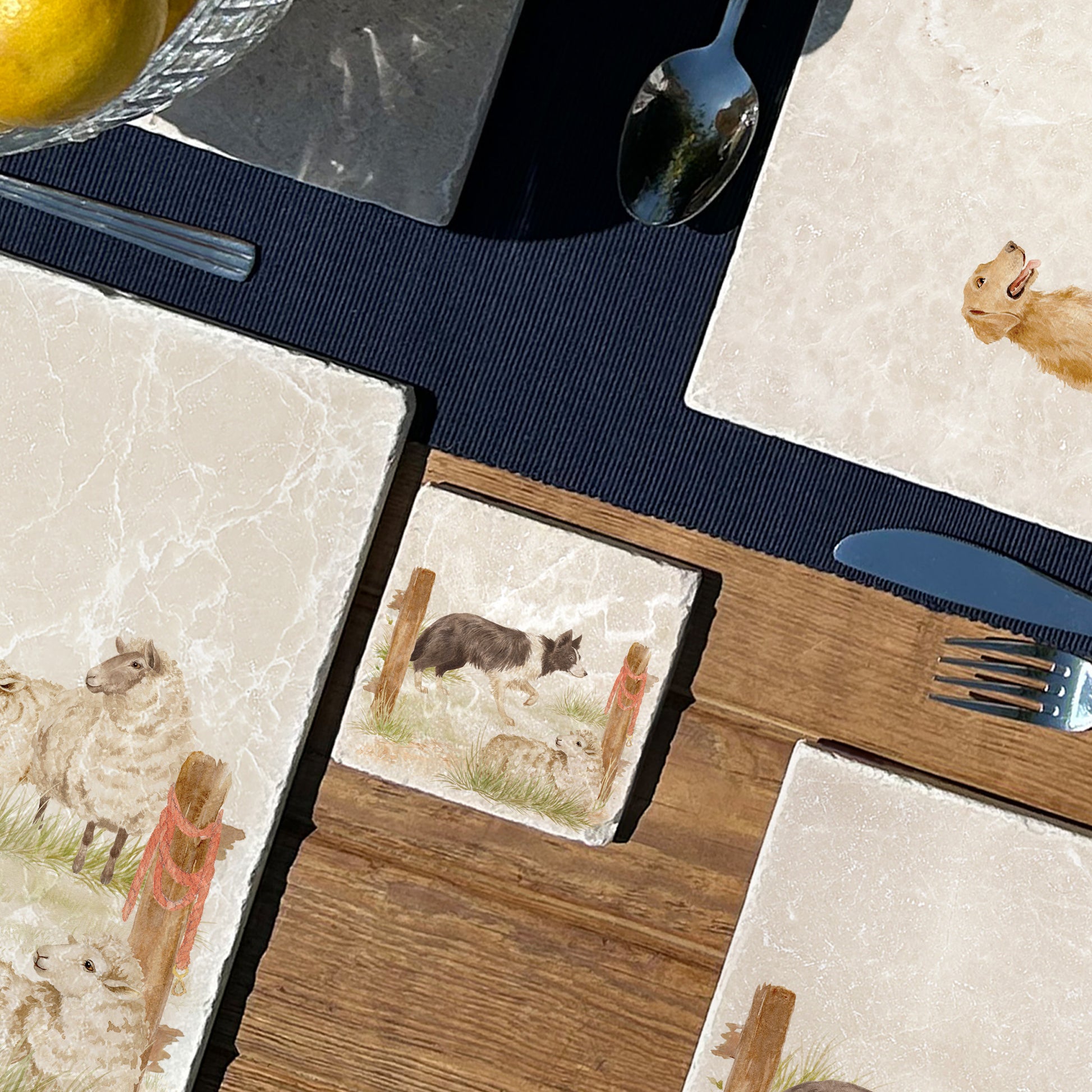 A square marble coaster with a design of a border collie working dog herding sheep through a gate on the farm. The coaster is set on a wooden country kitchen table.