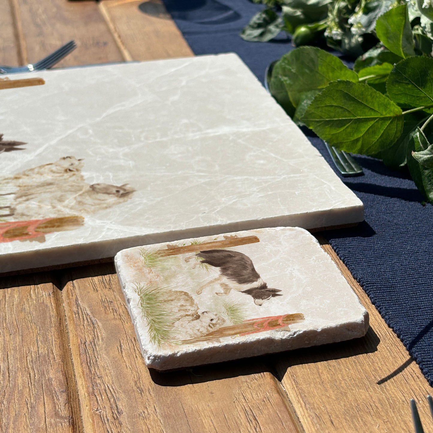 A square marble coaster with a design of a border collie working dog herding sheep through a gate on the farm. The coaster is set on a wooden country kitchen table.